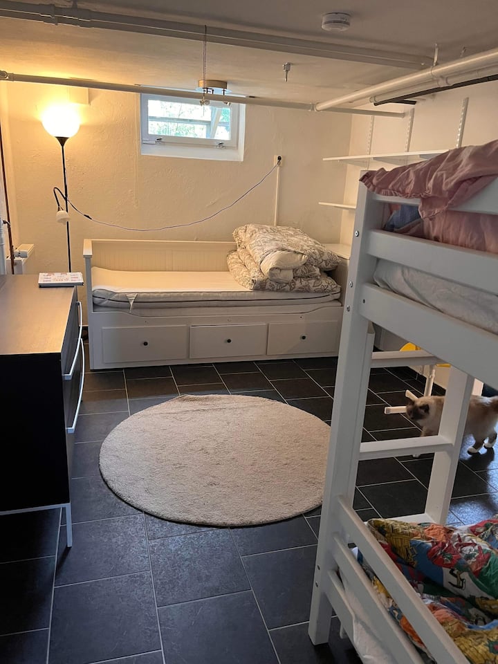 Chumba cha kulala kwenye chumba cha chini na kitanda cha mtu mmoja ambacho kinaweza kuvutwa kwenye kitanda cha watu wawili na kitanda cha ghorofa ndogo.