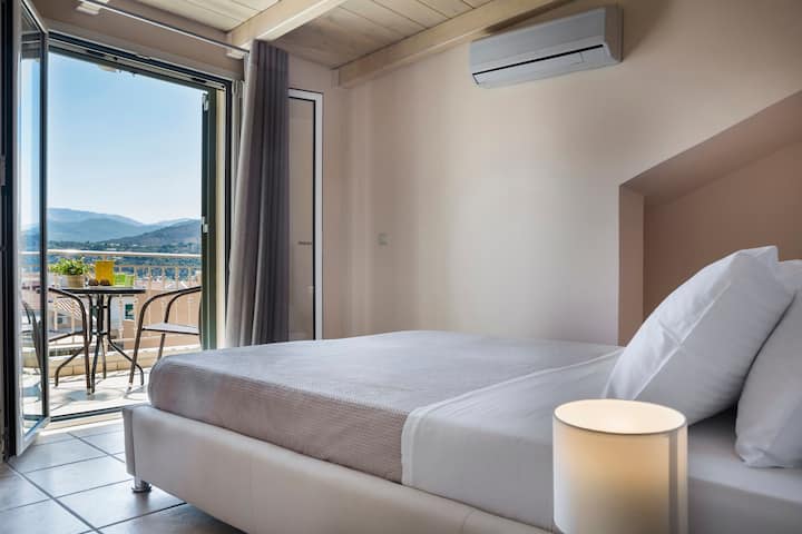 Kitanda cha watu wawili kilicho na roshani kinachoangalia milima na bandari kwenye mandharinyuma. A/C , Wodi zilizofungwa, kabati la kujipambia, meza ya usiku. Mapazia, luva halisi, vizuizi vya chuma. 