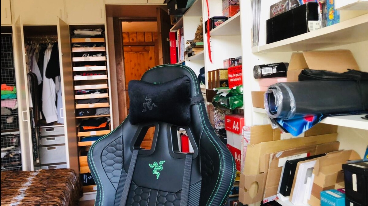A comfortable gaming chair is positioned in front of well-organized shelves filled with various items. A spacious wardrobe with a variety of clothing is visible in the background, contributing to an accessible living space.