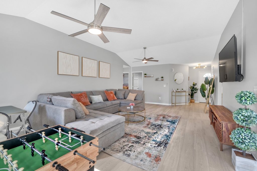 A spacious living area is highlighted by a large sectional sofa adorned with decorative pillows. A stylish coffee table centers the room, accompanied by a foosball table. A soft area rug adds warmth underfoot, while natural light fills the space through several windows.