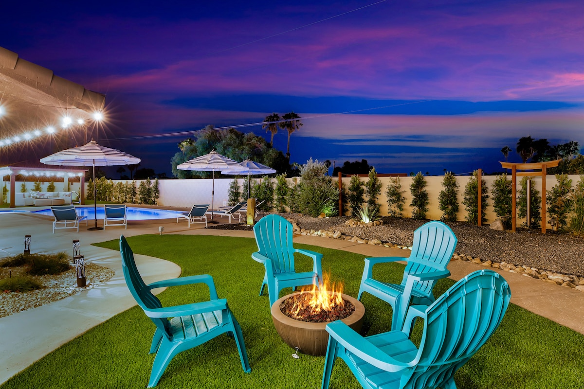 A serene outdoor space features a circular arrangement of teal lounge chairs around a fire pit, with a backdrop of a swimming pool and umbrellas. The evening sky showcases vibrant shades of purple, creating a tranquil atmosphere for relaxation.