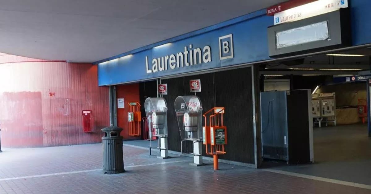 The entrance to the Laurentina B metro station is visible, featuring a prominent blue sign. Two payment machines are located on the left, with a trash bin nearby. The area is well-maintained, with a clean, tiled floor leading into the station.