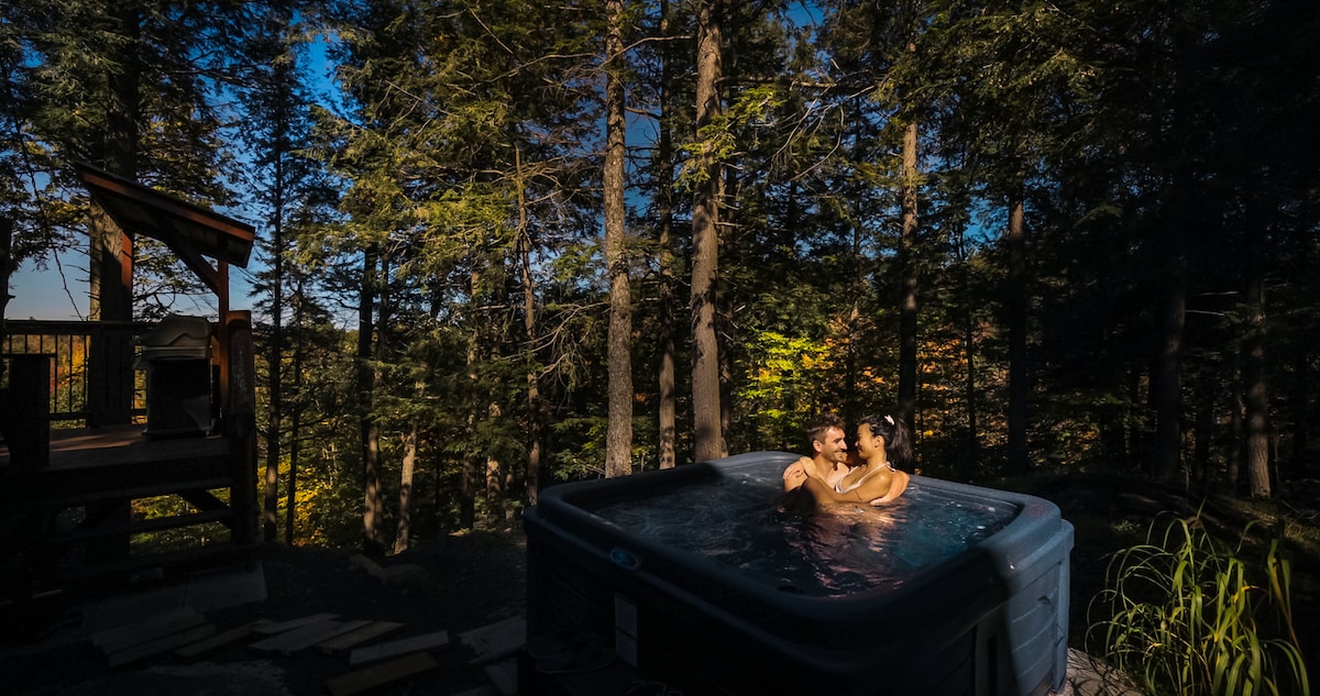 A hot tub is situated amidst tall trees, providing a serene setting for relaxation. The surrounding greenery enhances the connection to nature, with sunlight filtering through the foliage, creating a peaceful atmosphere for guests seeking tranquility.