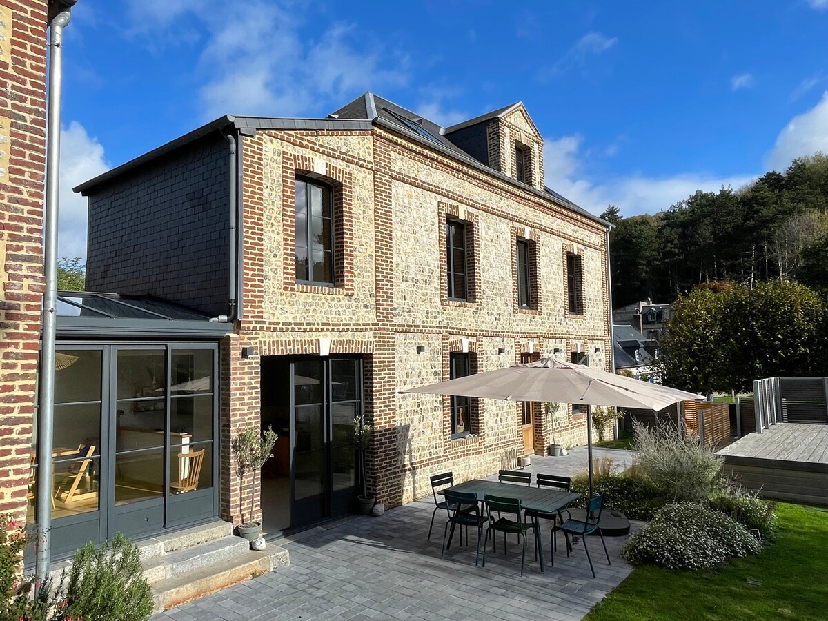 The exterior of the home features a blend of brick and board siding, showcasing large windows that invite natural light. A spacious patio area is highlighted, furnished with a dining table and umbrella, surrounded by landscaped greenery and maintained pathways.