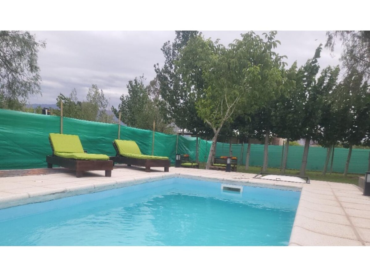 A refreshing outdoor pool is surrounded by comfortable lounge chairs with bright green cushions. Nearby trees and a fence provide a sense of privacy, while a grassy area invites guests to relax and enjoy the natural surroundings.