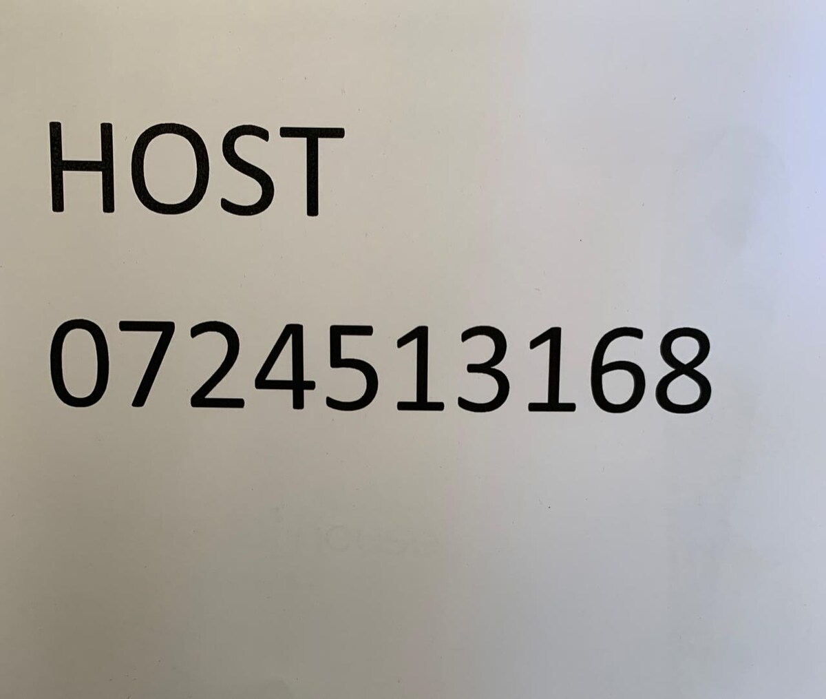 A sign displays the word 'HOST' in bold, uppercase letters above a contact number. The text is printed in a clear, sans-serif font, ensuring legibility. The background is plain, allowing the information to stand out.
