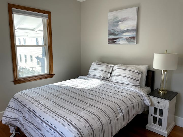 Cama tamaño queen con colchón Novafoam de 14pulgadas, una mesita de noche (carga junto a la cama equipada) y cortinas que oscurecen la habitación.