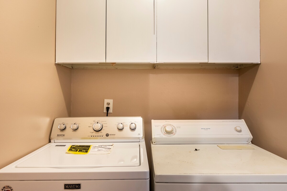 The laundry area features a stacked washer and dryer, positioned side by side. Above the appliances, there are shelves for storage. The walls are painted in a neutral tone, providing a simple backdrop for the essential laundry equipment.