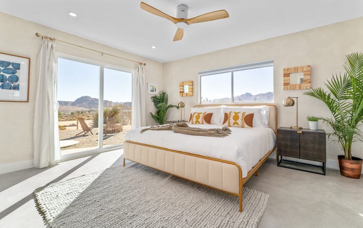 غرفة نوم رئيسية بسرير كينج وباب منزلق يؤدي إلى الفناء ومروحة سقف