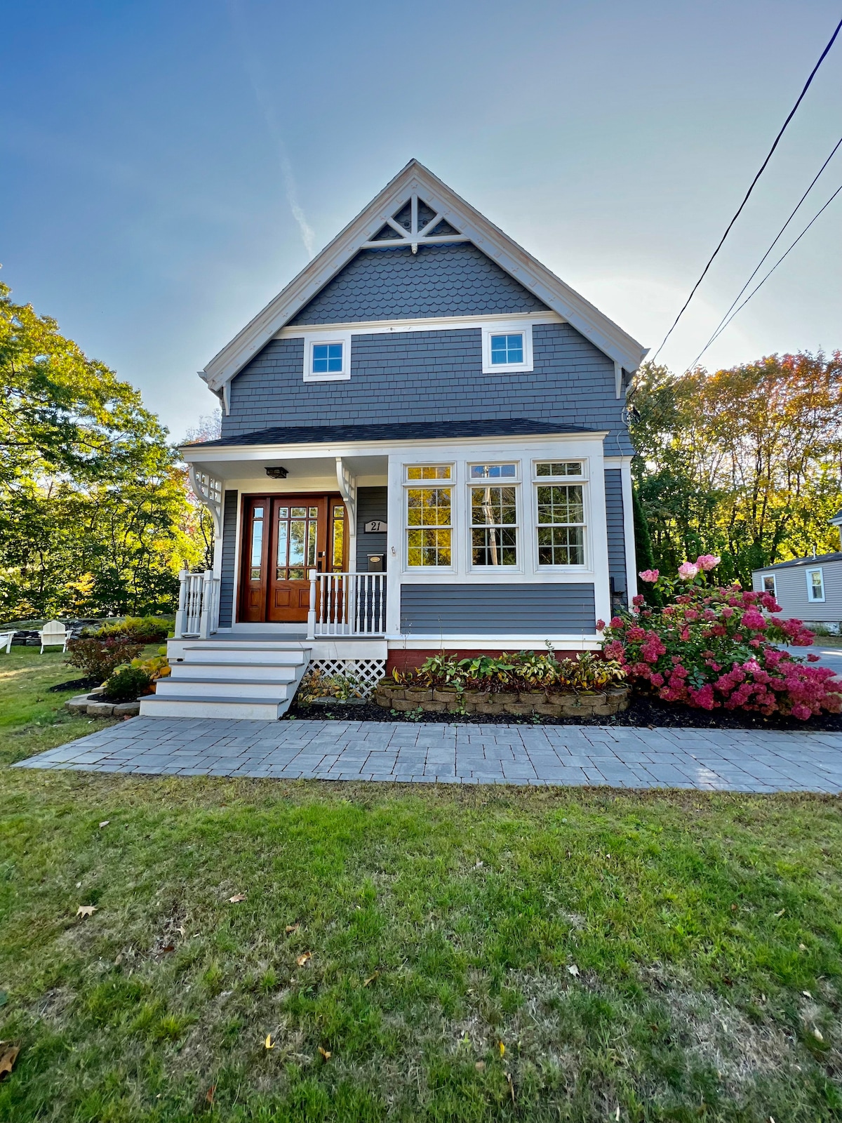 The exterior of the home displays a charming grey facade complemented by white trim and large front windows. Vibrant azaleas bloom along the walkway leading to the welcoming wooden front door. A well-manicured lawn enhances the inviting curb appeal.