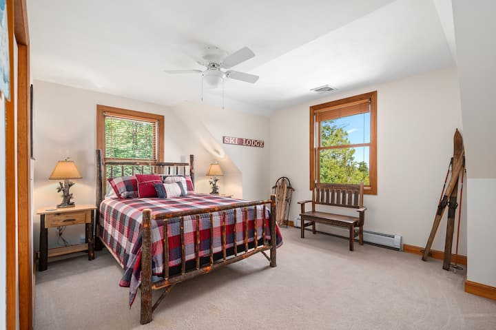 One of three upstairs bedrooms - this one features a queen bed, offering lovely views of the surrounding landscape with a cozy mountain lodge aesthetic with a solid wood bed frame, large windows, and plush carpeting.