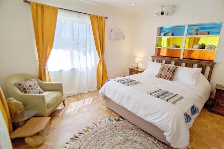 The master bedroom features scenic desert views with a queen size bed, a movie theater projector, a reading area with a stone table, and direct access to the bathroom, kitchen, and front patio.