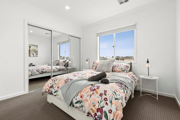 This bright and cheerful bedroom features a comfortable queen-sized bed, mirrored built-in robes, and a large window that fills the space with natural light, perfect for a restful retreat