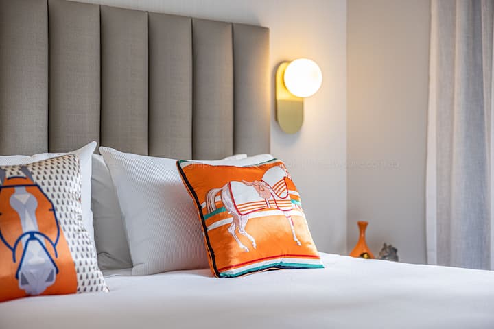 The bedroom features calming neutrals and natural tones, layered with soft furnishings and warm orange accents for a cosy, elegant retreat.