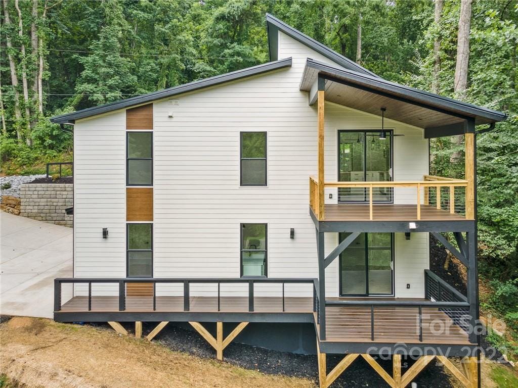 The modern guest suite is set in a serene wooded area, featuring a two-story design with large windows for natural light. A spacious private patio is visible, blending seamlessly with the outdoor environment. The entrance is accessible via a well-maintained driveway.