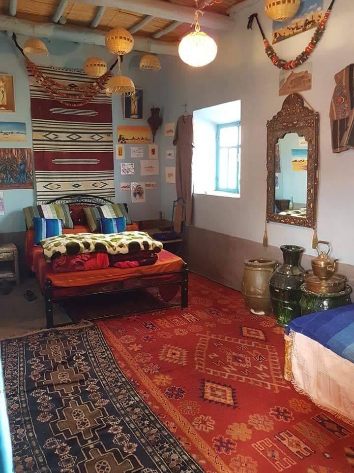 A warm bedroom space features traditional textiles and vibrant wall decor. A spacious bed is adorned with colorful blankets, and a large mirror reflects the room's intricate patterns. Elegant decorative jars and a rich area rug add to the inviting atmosphere.