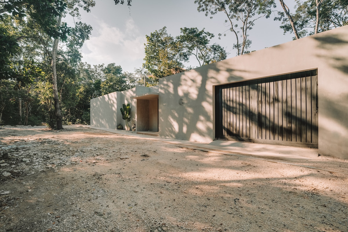 The exterior of the villa features a modern, minimalist facade with a large entrance and a garage. Surrounded by lush greenery, the structure blends harmoniously with the natural landscape, providing a serene and private atmosphere.