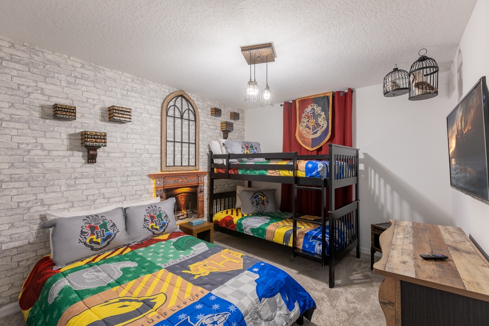 Plongez dans la magie de Poudlard dans cette chambre enchanteresse ! Un lit superposé double noir et un grand lit double sont habillés d'une literie vibrante et repos de maison sous un faux mur de pierre et une « fenêtre » voûtée.                                                       