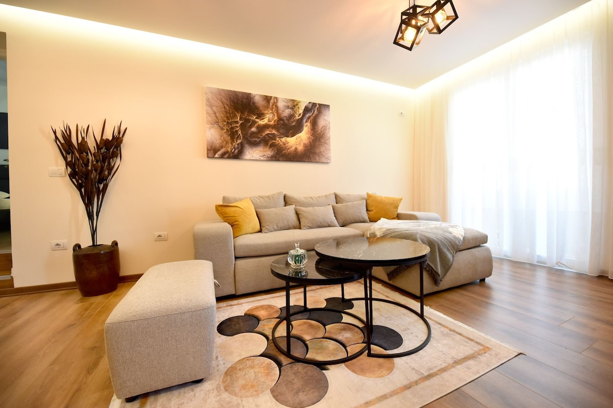 A modern living area is featured, showcasing a sectional sofa adorned with decorative pillows. A round coffee table is positioned on a patterned rug, enhancing the space's warmth. Soft natural light is allowed in through sheer curtains, illuminating the room's neutral tones.