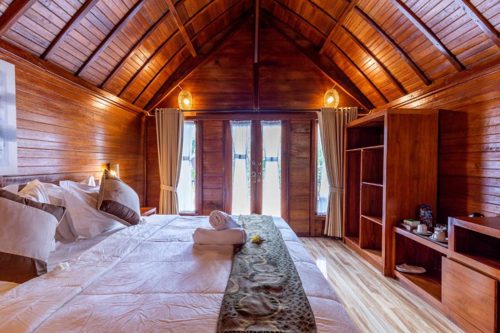 A cozy and inviting bedroom features a double bed dressed in crisp linen. Wooden walls and high ceilings are highlighted by warm lighting. Large doors open to an outdoor view, and a small seating area with a tea and coffee station is positioned nearby.