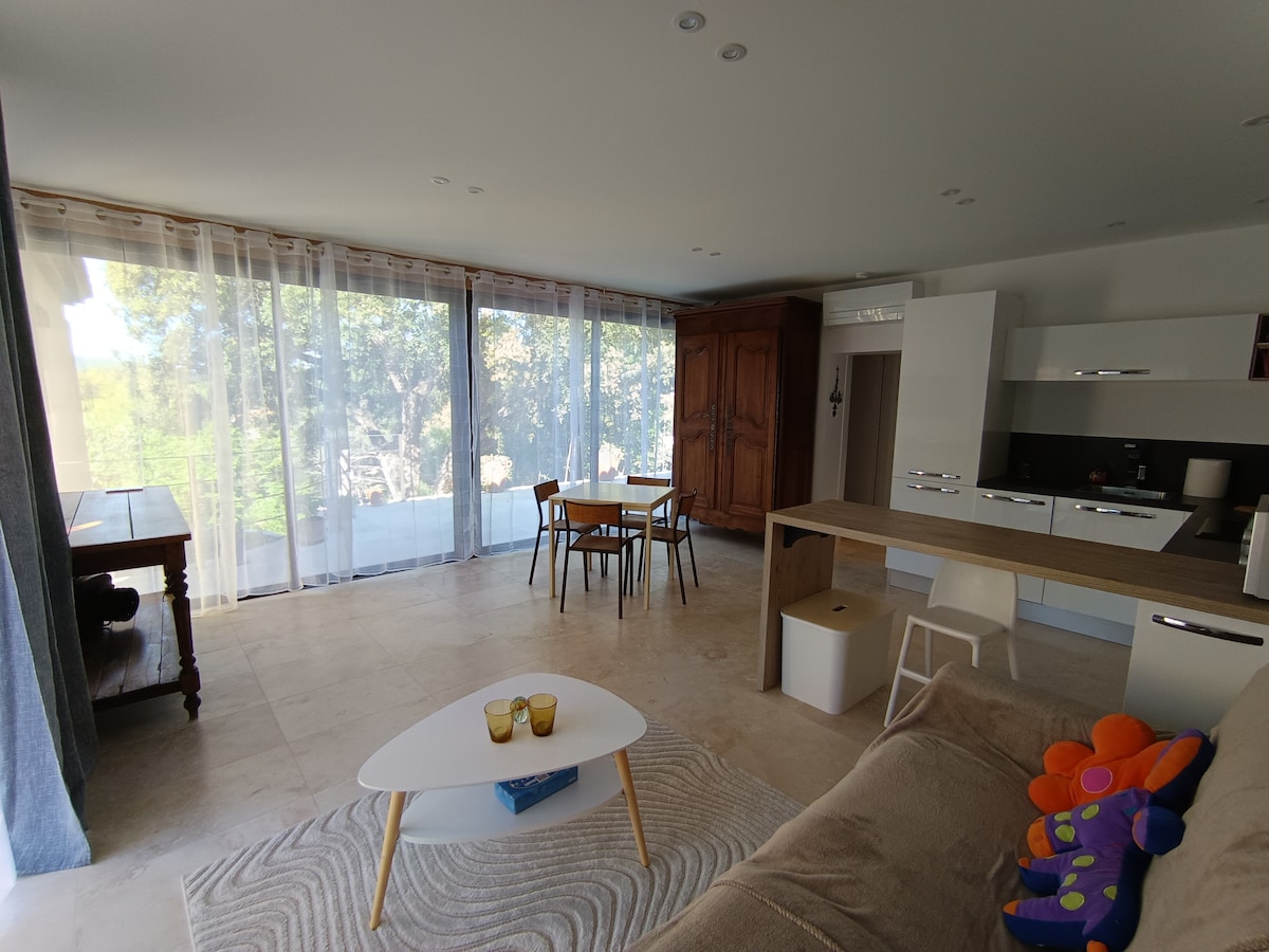 The living area is characterized by large windows that allow natural light to fill the space. A spacious sofa faces a low coffee table, while a dining table with chairs is positioned nearby. A wooden cabinet adds a touch of warmth to the modern décor.