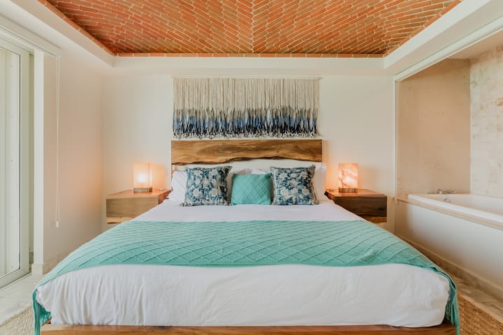 Chumba cha kulala cha kifahari chenye kitanda cha mfalme kilicho na ubao wa kichwa uliotengenezwa kwa mikono, dari ya matofali na mwanga wa joto.