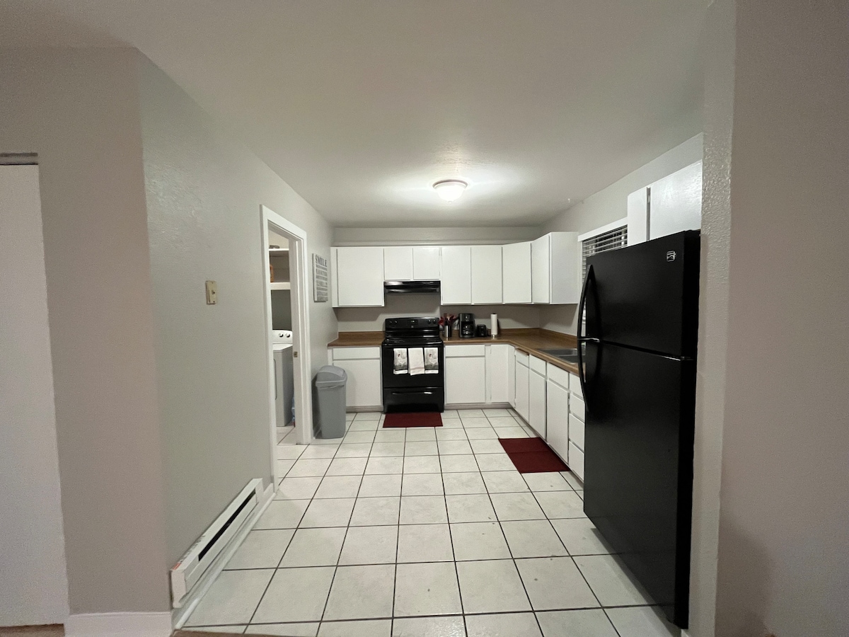 The kitchen features white cabinetry paired with a black refrigerator and an oven range. A spacious layout is highlighted by tiled flooring and ample countertop space. Laundry facilities are visible through a doorway, contributing to a practical environment.