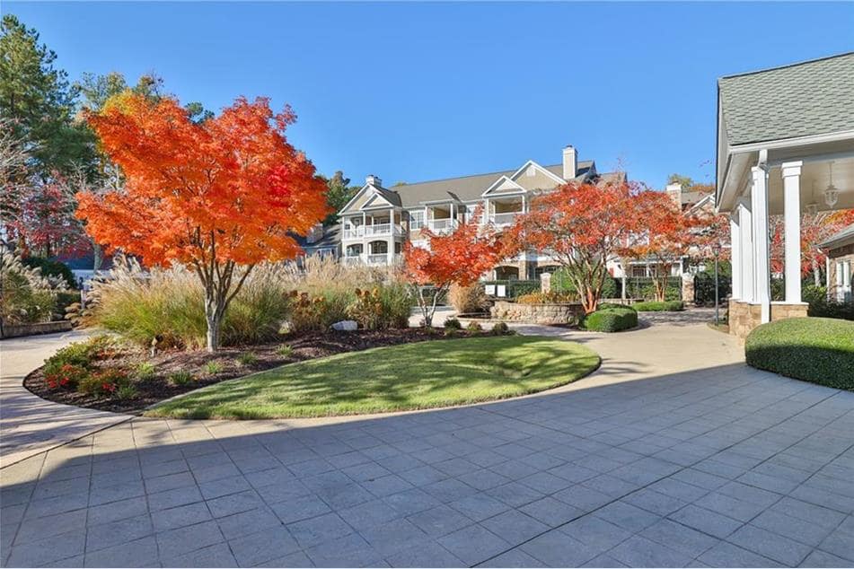 A well-maintained outdoor area showcases a pathway lined with neatly manicured grass and colorful trees displaying vivid autumn foliage. The backdrop features a multi-story building, accentuating the serene and clean environment of the community.