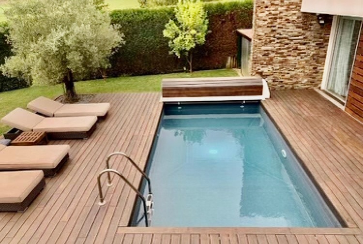 An inviting outdoor space features a private swimming pool surrounded by wooden decking. Several loungers are positioned nearby for relaxation, and lush greenery borders the area, providing a sense of tranquility. The pool is well-lit, enhancing its appeal for evening enjoyment.