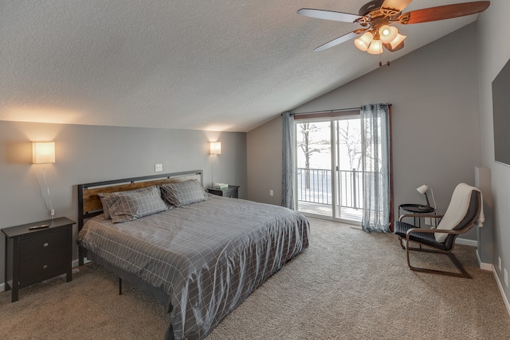 Lower bedroom with king bed, balcony, tv, and reading chair.