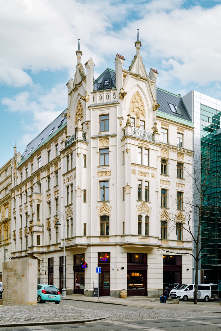 The building features intricate architectural detailing with ornate elements, including pointed arches and decorative stonework. Large windows adorn the façade, allowing for ample natural light. The contemporary structure on the right contrasts with the historic design, showcasing a blend of old and new architecture.