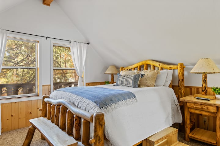 The Master bedroom upstairs with natural log furniture, nightstand and lamp on each side of the bed, bench seat for changing clothes, 26in wall mounted TV with Spectrum cable, a large closet for storage, and a ceiling fan