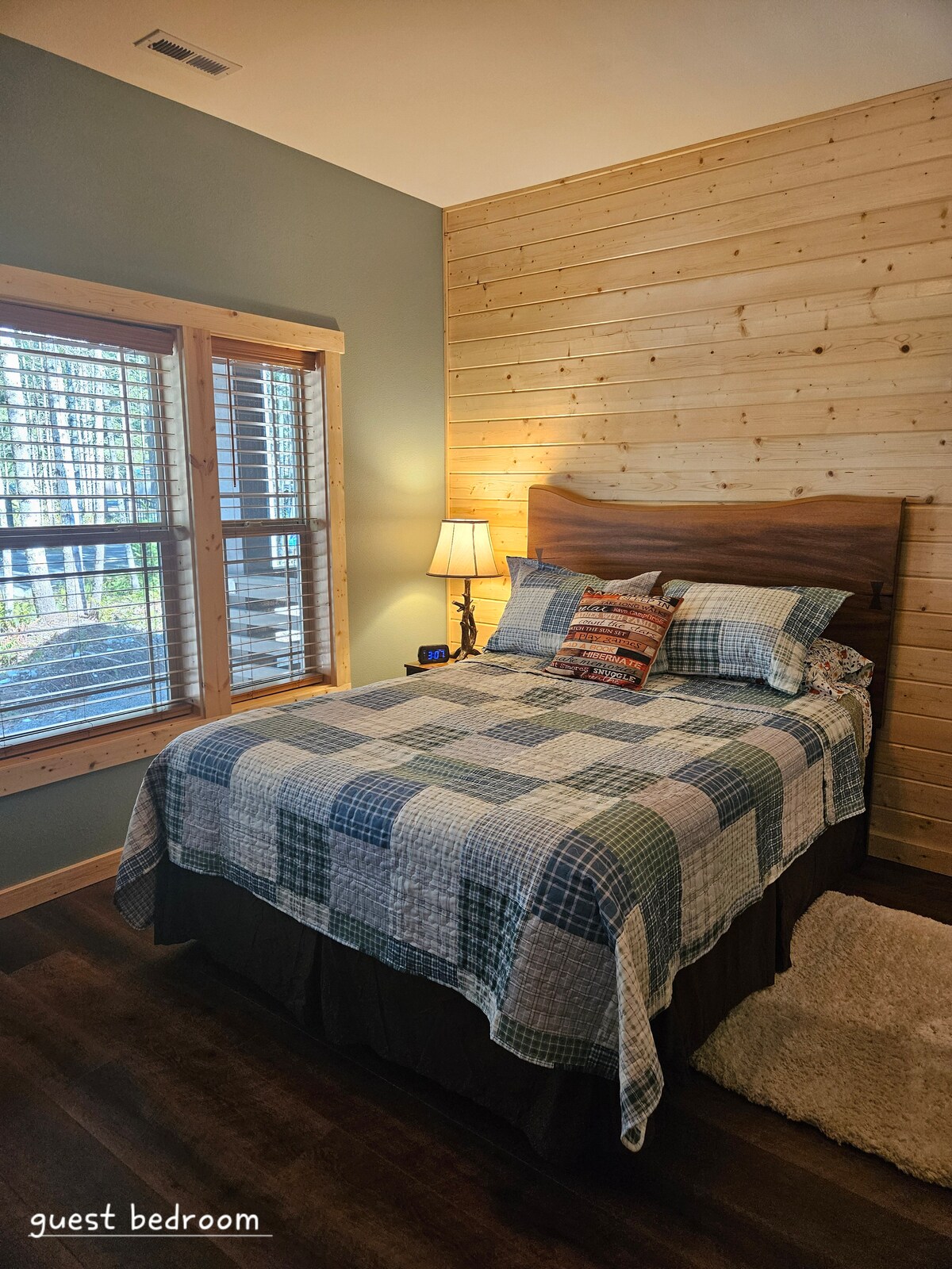 Queen size bed with table, lamp, and alarm clock.