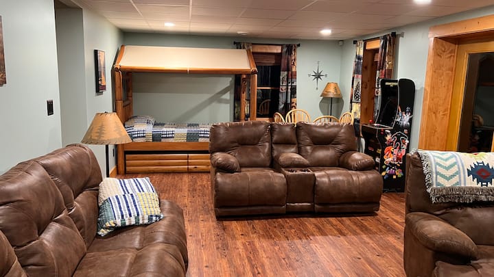 Fun family room in basement with reclining sofas, dining table for games, twin log bed with twin trundle and arcade game.