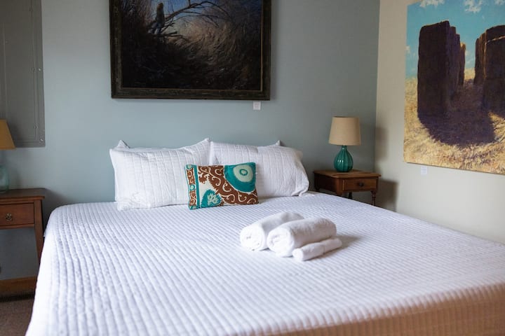 Dormitorio de la planta baja con una cama tamaño king y arte local.