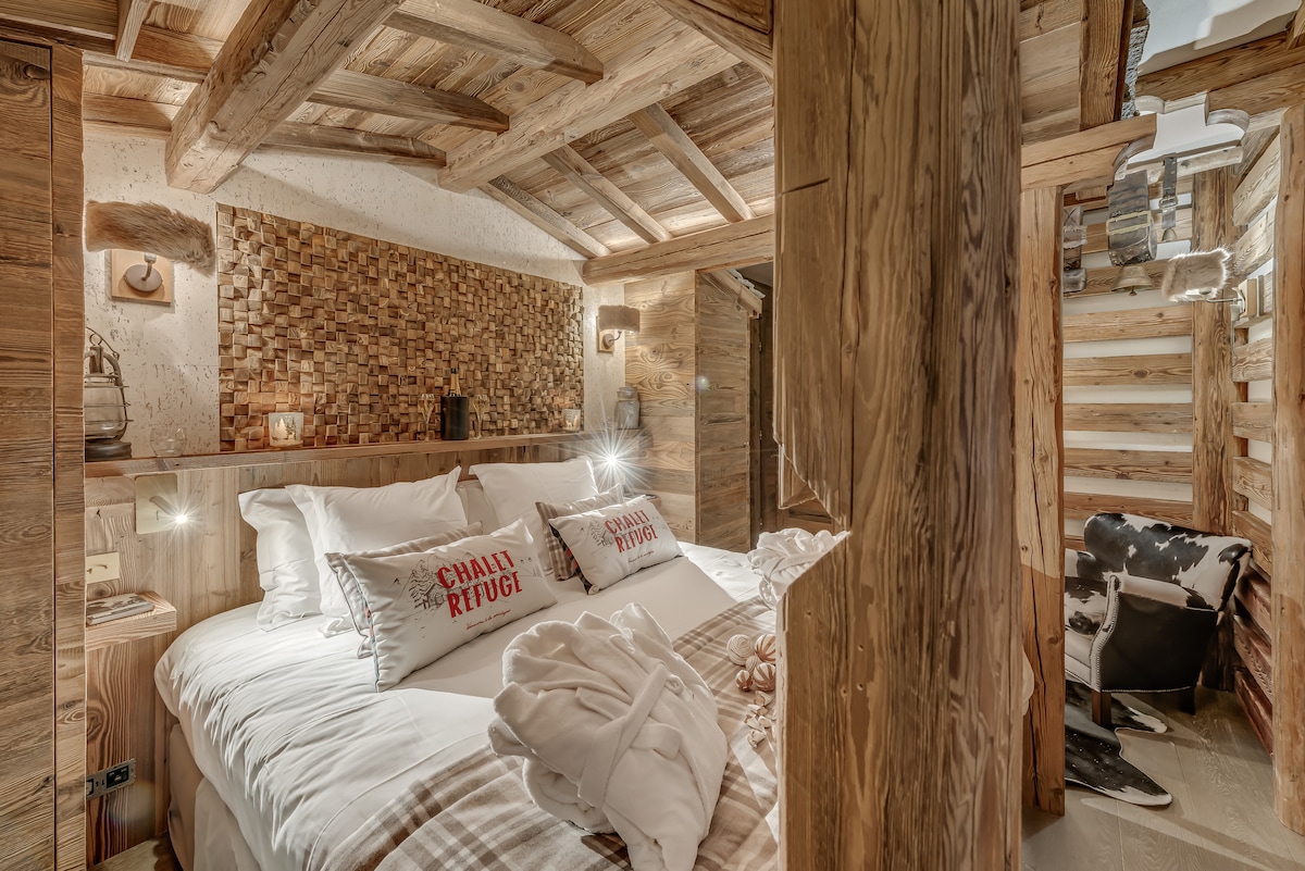 Habitación "Refugio" 
Le sumerge en el ambiente cálido y auténtico de un antiguo refugio de montaña. Las paredes adornadas con viejas campanas, un verdadero techo de lauze... un cómodo sillón de piel recrea un espacio lleno de encanto.