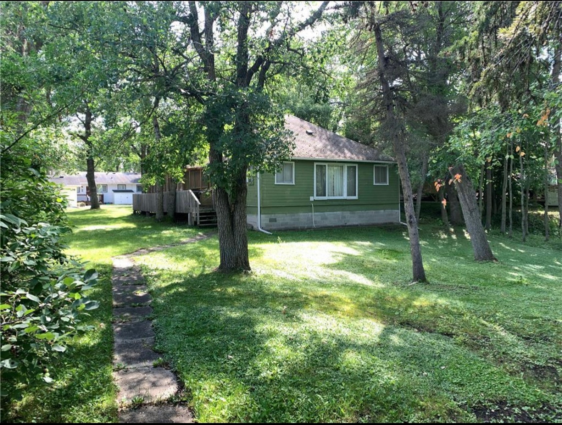 A spacious green yard surrounds a charming cabin, providing a serene atmosphere. The cabin features large windows that allow natural light to enter. Mature trees add shade, while a stone pathway leads to the entrance, creating an inviting approach to the property.