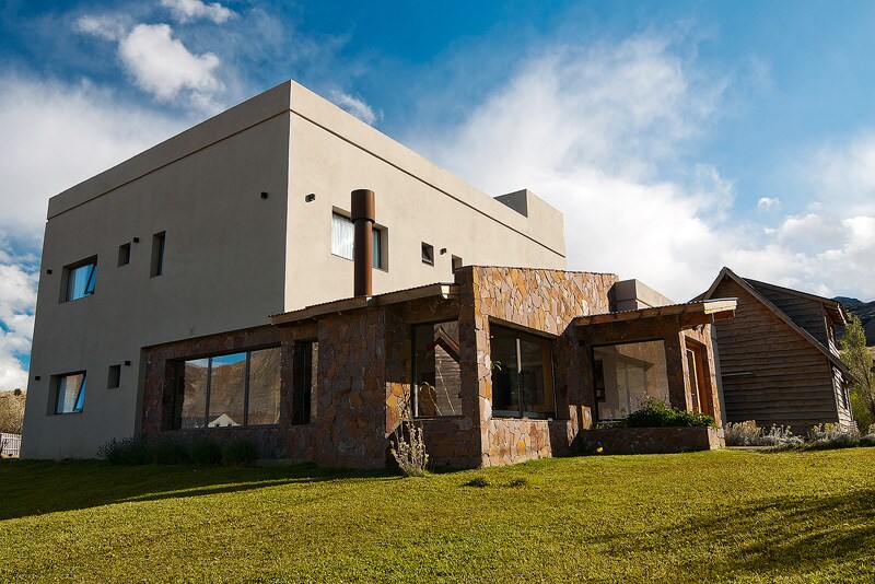 A modern building with a stone and stucco exterior is showcased, featuring large windows that allow natural light to fill the interior. The surrounding green lawn and mix of textures contribute to a harmonious setting.