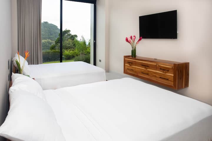 Descubre la tranquilidad en nuestro acogedor dormitorio con dos camas tamaño queen, una puerta corrediza de cristal que se abre al exuberante jardín y un televisor grande para que disfrutes.
