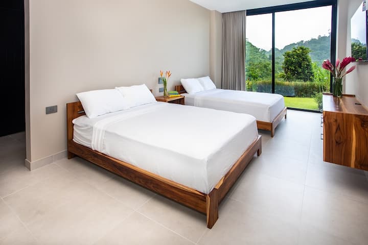 Descubre nuestro acogedor dormitorio con dos camas tamaño queen, que ofrece acceso directo al exuberante jardín tropical. Disfruta de la relajante vista al mar desde la comodidad de tu habitación.
