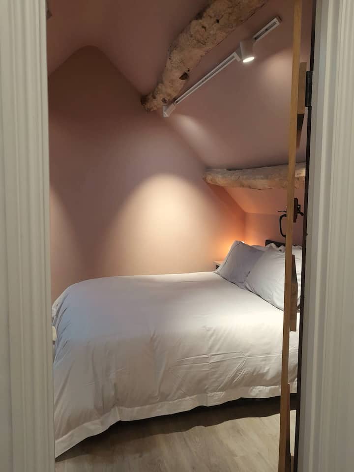 ห้องนอนคอกม้าที่มีเพดานโค้งและคานไม้โอ๊คเดิม เตียงเป็นสไตล์ออตโตมันซึ่งเปิดออกเพื่อเก็บกระเป๋าเดินทางด้านล่าง