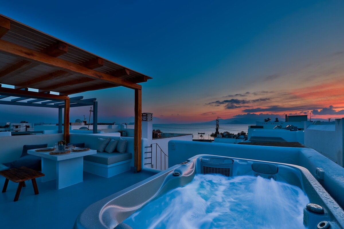A private rooftop terrace is highlighted, featuring a hot tub surrounded by a wooden pergola. Comfortable seating and a dining area are included, with a panoramic view of the sea and a colorful sunset enhancing the serene atmosphere.