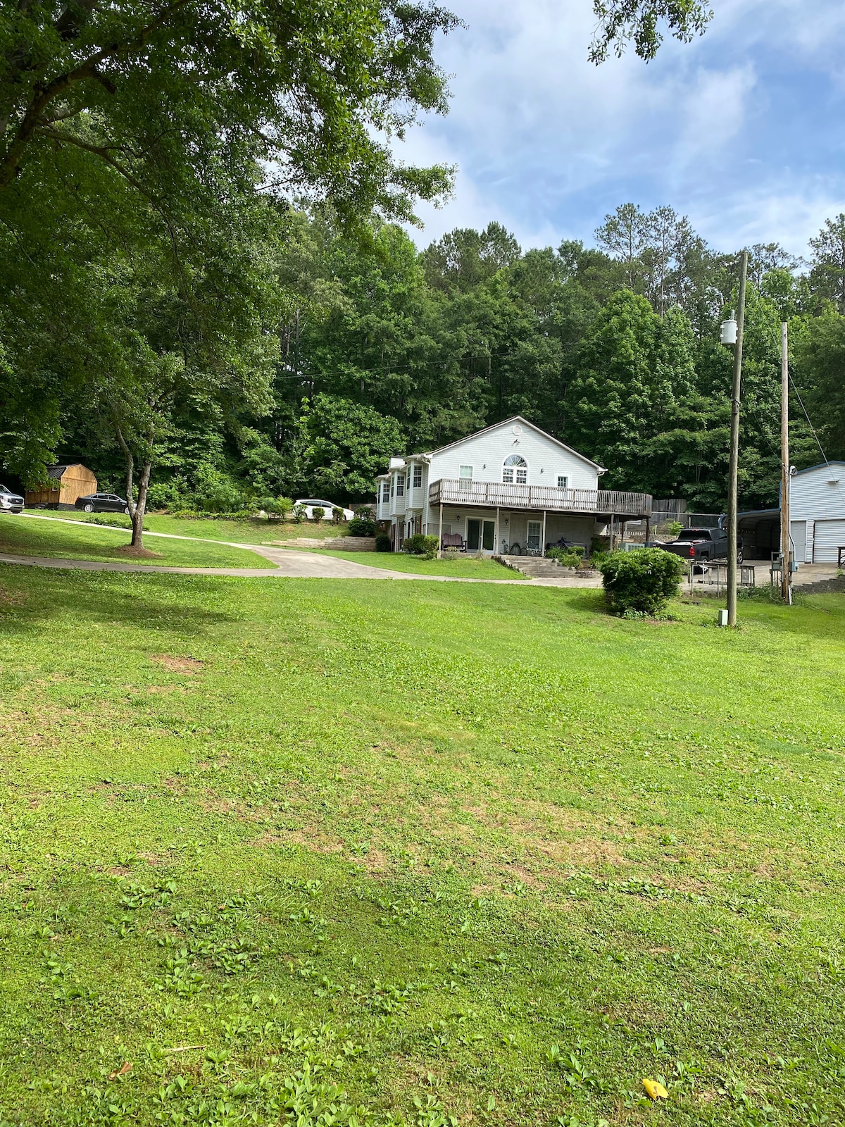 A well-maintained house is set against a backdrop of lush greenery, surrounded by a spacious lawn. The building features multiple levels and a deck, allowing for outdoor relaxation. Trees provide natural shade in a tranquil environment, enhancing the connection to nature.