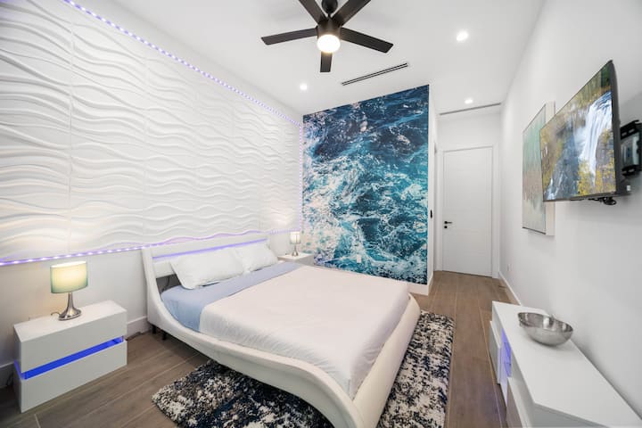 Chumba cha kulala cha kisasa kilichohamasishwa na bahari chenye ukuta wa wimbi laini, kitanda cha kifalme chenye starehe, taa ya LED ya mazingira na televisheni janja, kinafaa kwa mapumziko tulivu na maridadi