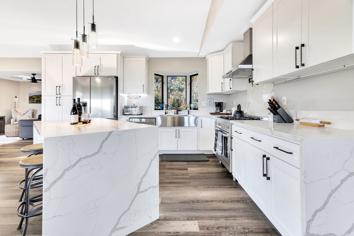 The kitchen features modern cabinetry and stainless steel appliances, with a spacious island offering seating. Natural light filters through windows, highlighting the sleek countertops and contemporary finishes. The layout creates an inviting atmosphere for meal preparation and casual gatherings.