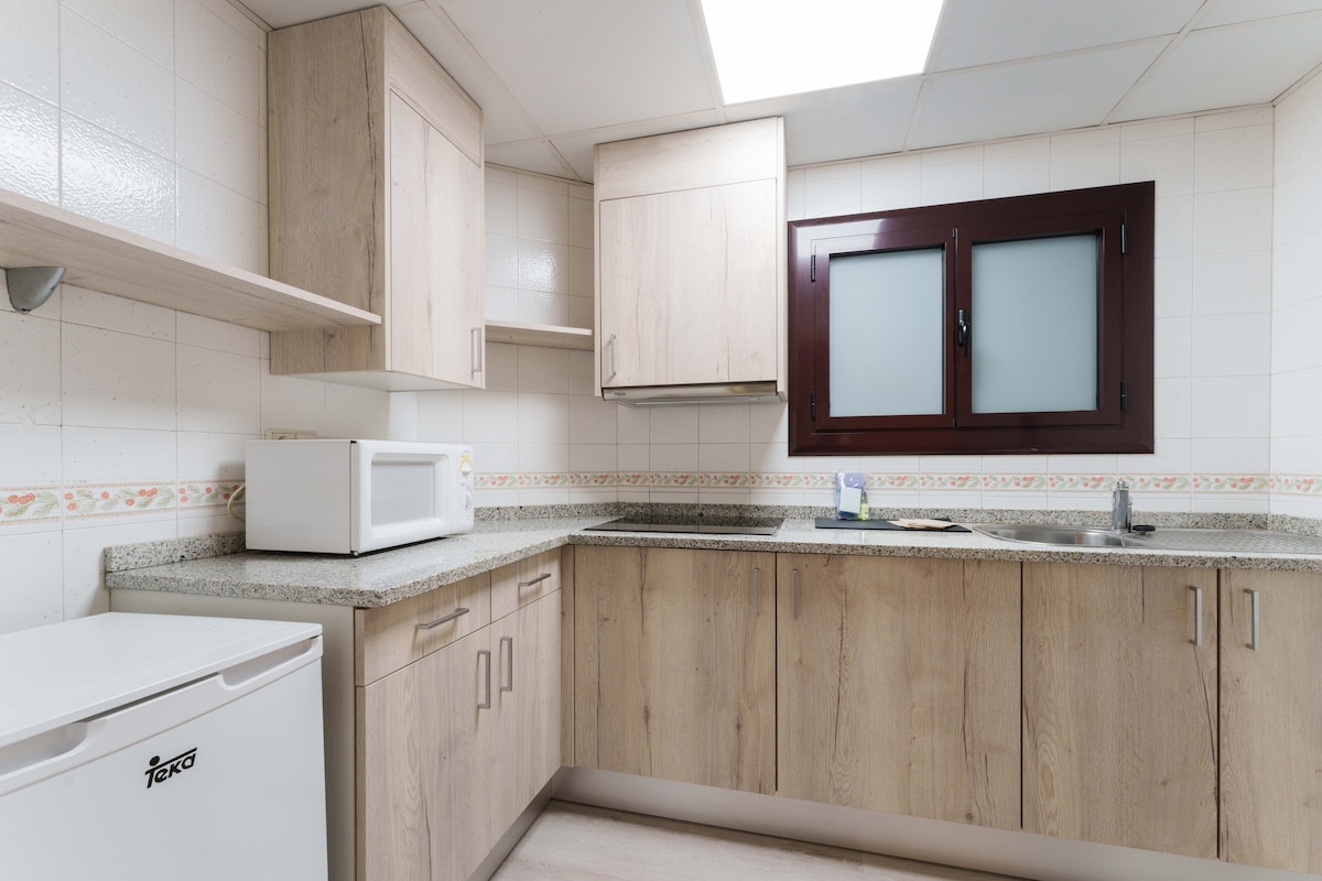 A functional kitchen area is showcased, featuring light wood cabinetry and granite countertops. A microwave and refrigerator are included for convenience. A window allows natural light into the space, while a neutral tile backsplash complements the overall design.