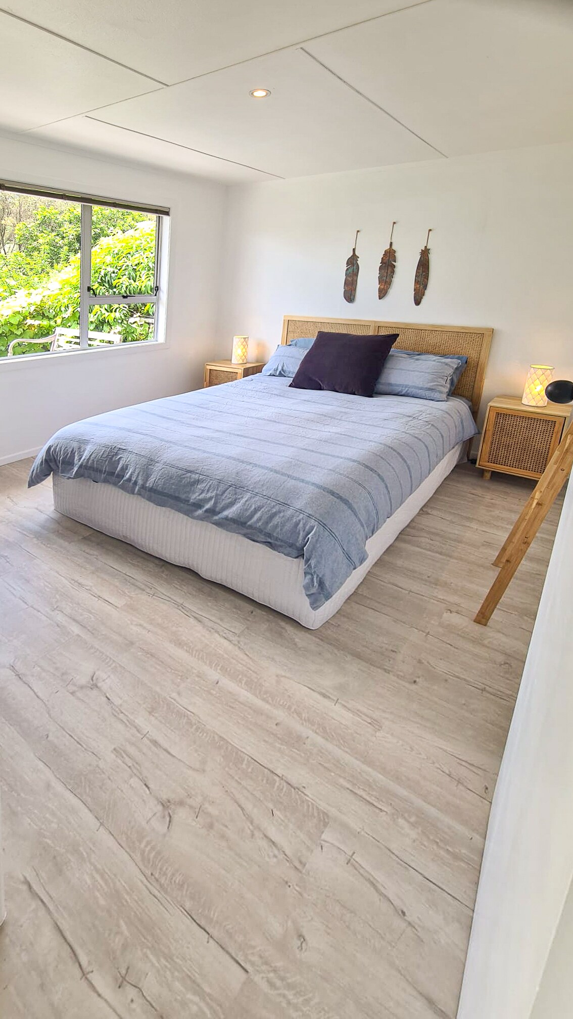 The Master bedroom, generous size with a queen bed this light-filled space views out to the native bush and garden. Side tables, table lamps, a clothes storage rack and a make up mirror.