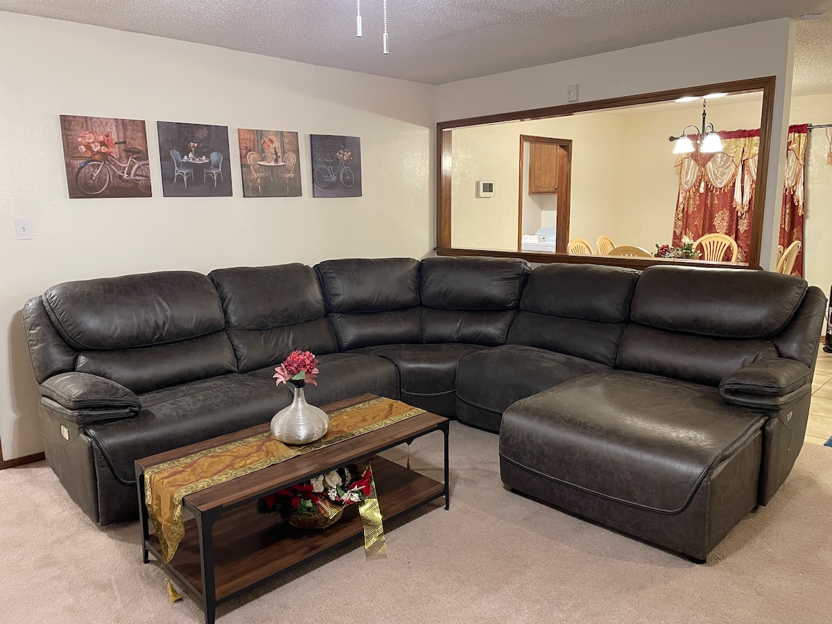 A sectional sofa in dark leather offers seating for multiple guests, positioned near a low coffee table adorned with a vase of flowers. Above the sofa, four framed images of bicycles add a decorative touch to the wall, complementing the cozy living space.
