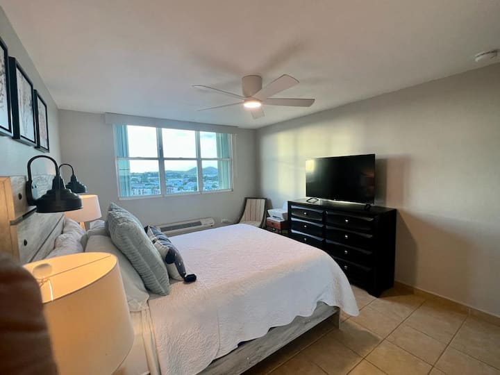 宽敞宁静的卧室，配备全尺寸床、柔软床单、吊扇和平板电视，为您提供舒适的放松和充电空间。