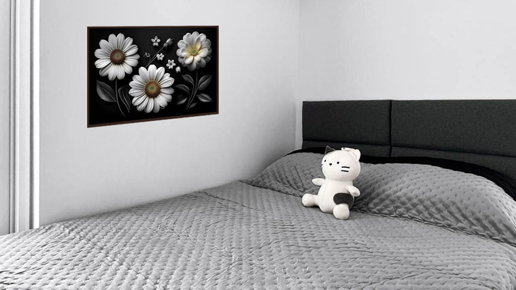 A spacious bed with a black, upholstered headboard is covered in a textured gray quilt. A framed floral artwork decorates the wall above, featuring white daisies. A plush toy rests on the bed, adding a touch of warmth to the minimalist setting.